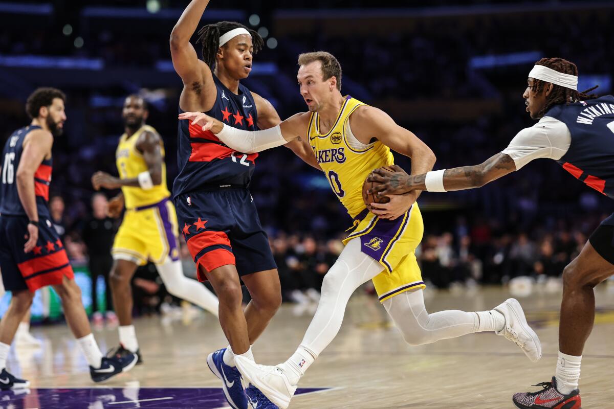 Lakers guard Luke Kennard, center, drives between Washington's Tre Johnson, left, and Jamir Watkins.