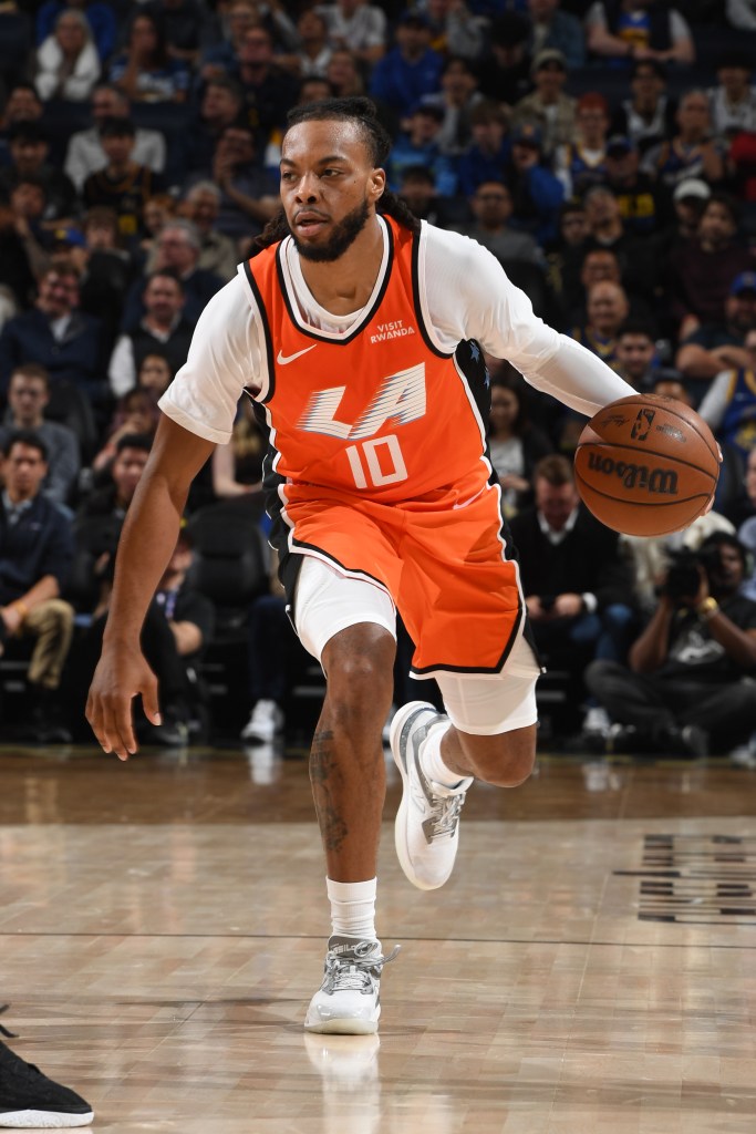 A male basketball player in an orange and white uniform dribbles a basketball on a court.