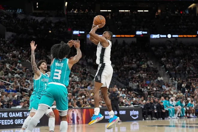 Mar 14, 2026; San Antonio, Texas, USA; San Antonio Spurs guard De'aaron Fox (4) shoots over Charlotte Hornets guards LaMelo Ball (1) and Coby White (3) in the second half at Frost Bank Center.