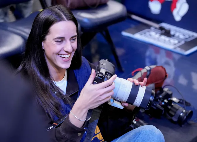 Indiana Fever guard Caitlin Clark sits on the baseline with a camera Wednesday, March 25, 2026, ahead of a game against the Los Angeles Lakers at Gainbridge Fieldhouse in Indianapolis.