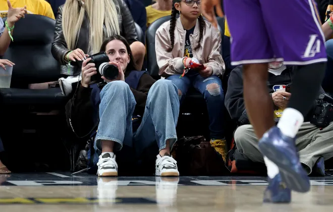 INDIANAPOLIS, INDIANA - MARCH 25: Caitlin Clark of the Indiana Fever sits on the baseline and makes photographs during the Indiana Pacers game against the Los Angeles Lakers at Gainbridge Fieldhouse on March 25, 2026, in Indianapolis, Indiana. NOTE TO USER: User expressly acknowledges and agrees that, by downloading and or using this photograph, User is consenting to the terms and conditions of the Getty Images License Agreement (Photo by Andy Lyons/Getty Images)