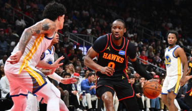 A Hawks player dribbles the basketball toward the basket while being guarded by two Warriors players on a basketball court.