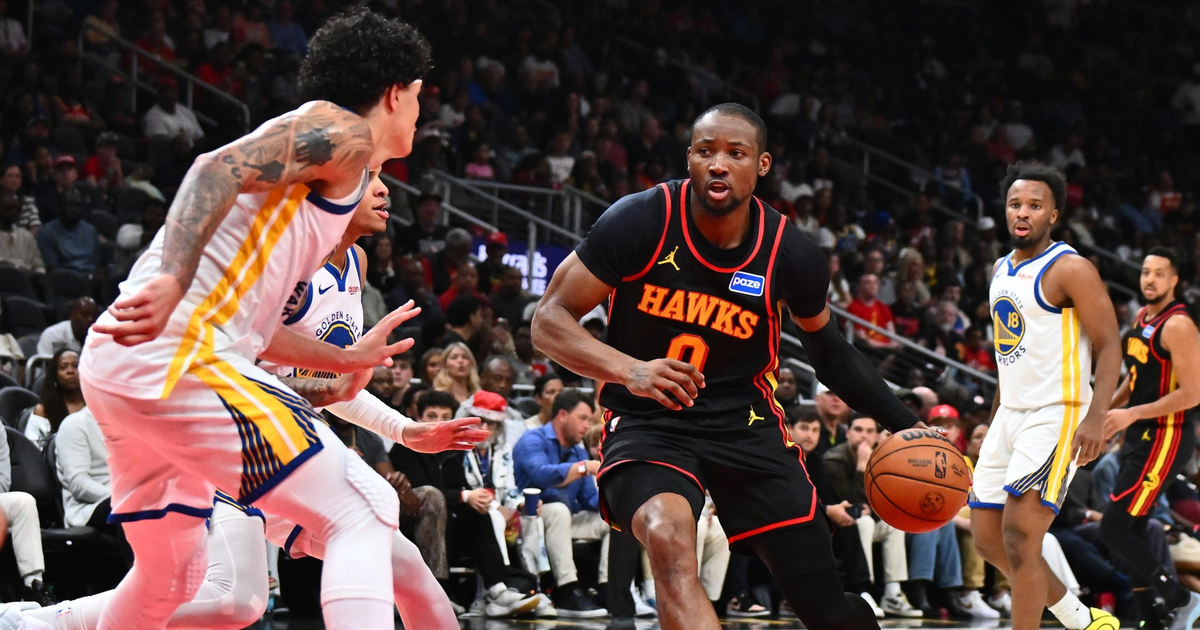 A Hawks player dribbles the basketball toward the basket while being guarded by two Warriors players on a basketball court.