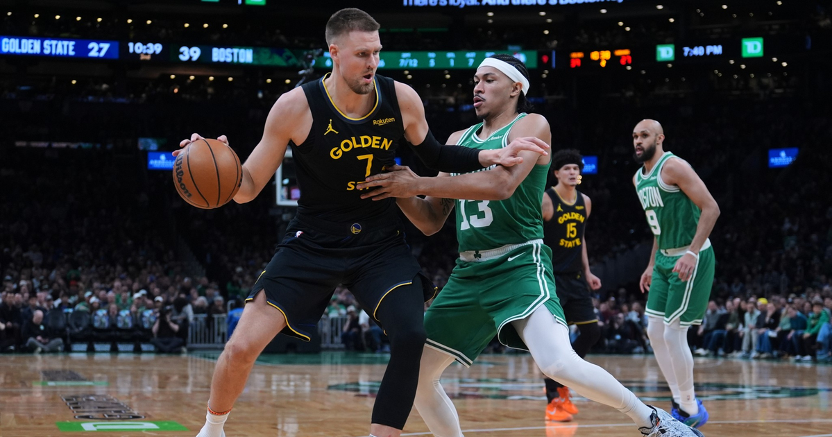 A Golden State player holds the basketball while defending against a Boston player in green during a lively basketball game.