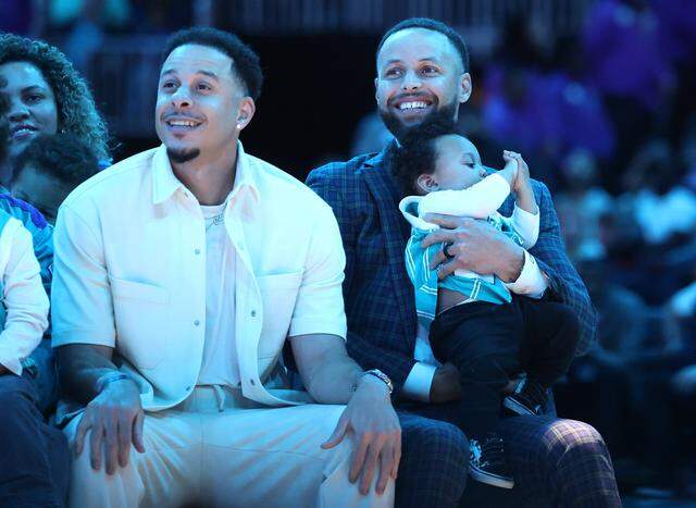 NBA players Seth and Steph Curry smile as they listen to their father and Charlotte Hornets forward Dell Curry speak during his jersey retirement ceremony at Spectrum Center on Thursday, March 19, 2026. The Charlotte Hornets retired Dell Curry's number 30 jersey and lifted a banner into the rafters during half time of the team's game against the Orlando Magic.