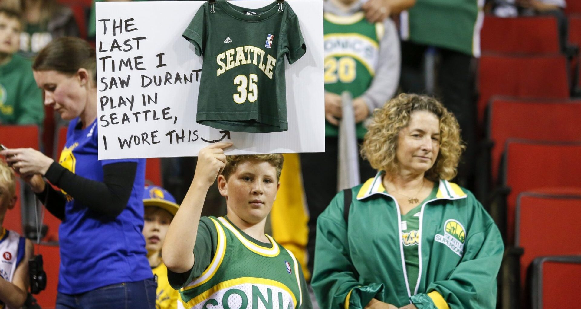 Oct 5, 2018; Seattle, WA, USA; Seattle Supersonics fan Ervin Fleshman of Edison, Washington holds a sign with his mother Allison (right) during pregame warmups for a game between the Golden State Warriors and Sacramento Kings at KeyArena.