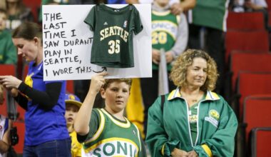 Oct 5, 2018; Seattle, WA, USA; Seattle Supersonics fan Ervin Fleshman of Edison, Washington holds a sign with his mother Allison (right) during pregame warmups for a game between the Golden State Warriors and Sacramento Kings at KeyArena.