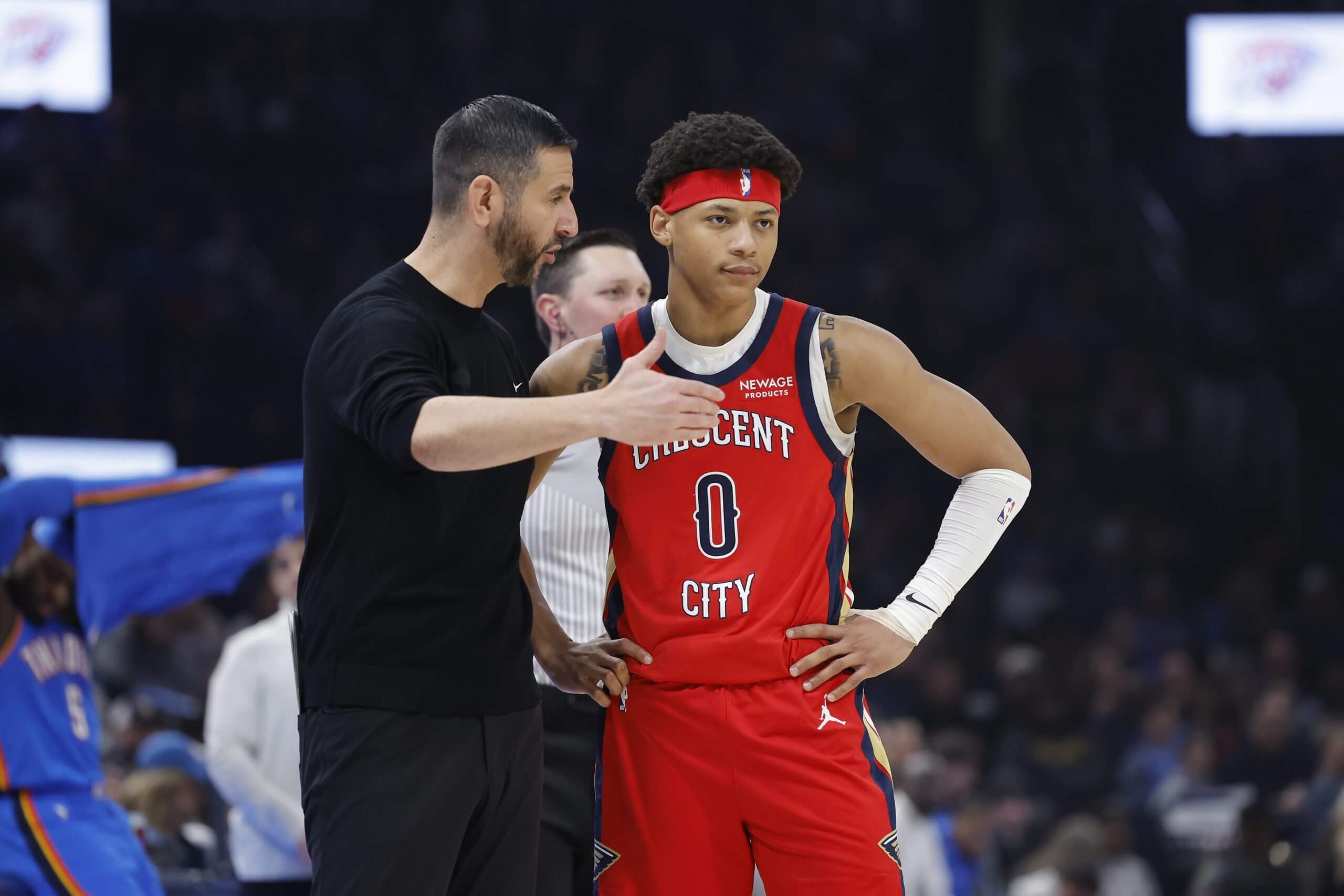 An image of New Orleans Pelicans coach James Borrego speaking to point guard Jeremiah Fears on the sideline during an NBA game.