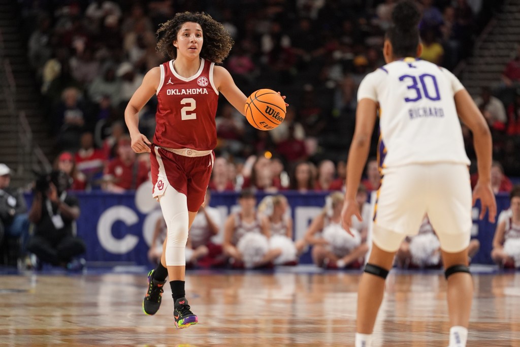 Oklahoma guard Aaliyah Chavez dribbles the ball. The ball is in her hand, and an LSU defender is standing in front of her, facing her.
