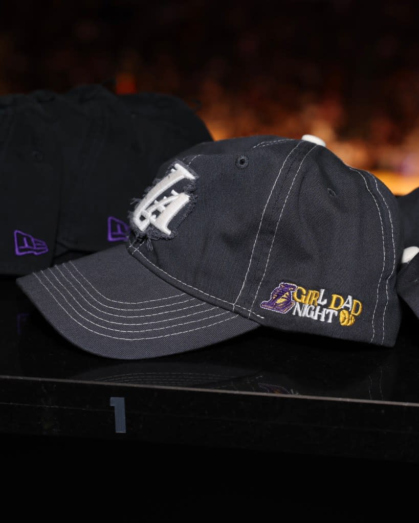 A black baseball cap with white stitching on the brim, featuring a white “L” logo and “GIRL DAD NIGHT” in yellow and white text, on a black surface.