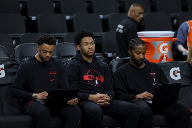 Chicago Bulls guard Anfernee Simons sits on the sideline with Bulls staff members Isiah Price, left, and Micah Burno, right, before a game against the Los Angeles Clippers on Friday, March 13, 2026, in Inglewood, Calif. (AP Photo/Ryan Sun)
