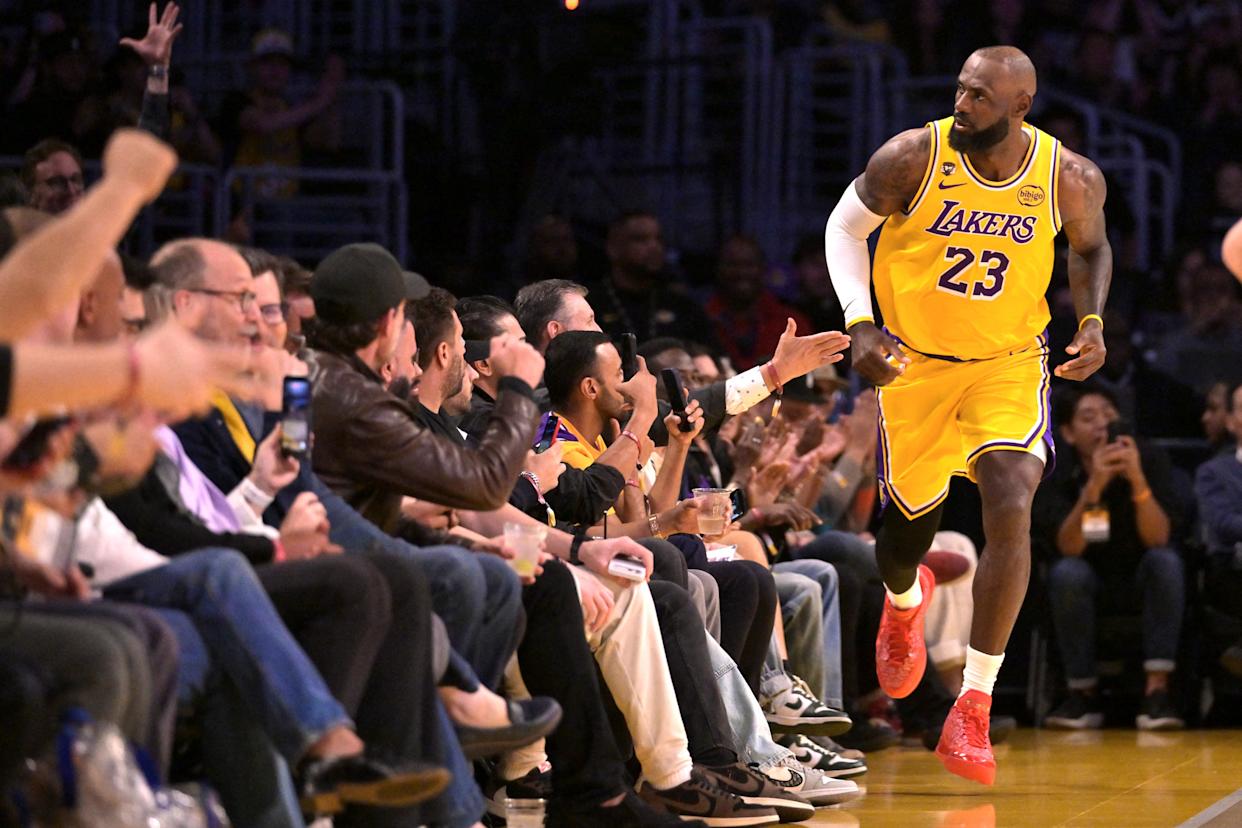 LeBron James in a yellow Lakers uniform running past fans courtside.
