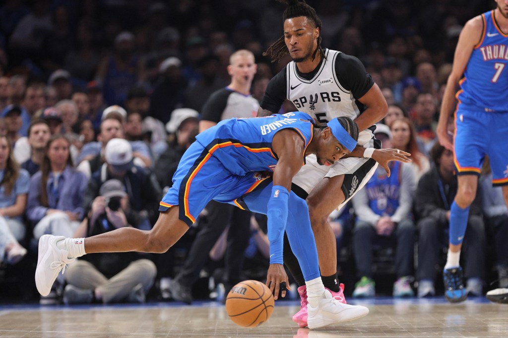 Oklahoma City Thunder guard Shai Gilgeous-Alexander, center, tries to keep control of the ball against San Antonio Spurs guard Stephon Castle (5). 