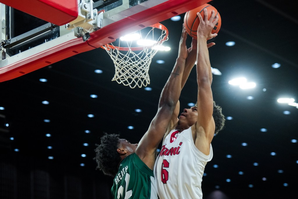 Two basketball players reach for a rebound under the basket.