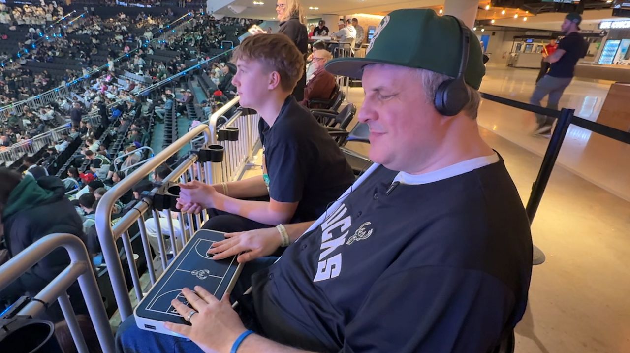 Steve Heesen and his son at a Bucks game. Heesen is using a tactile broadcast device to follow along with the game. (Abbey Taylor/Spectrum News 1)