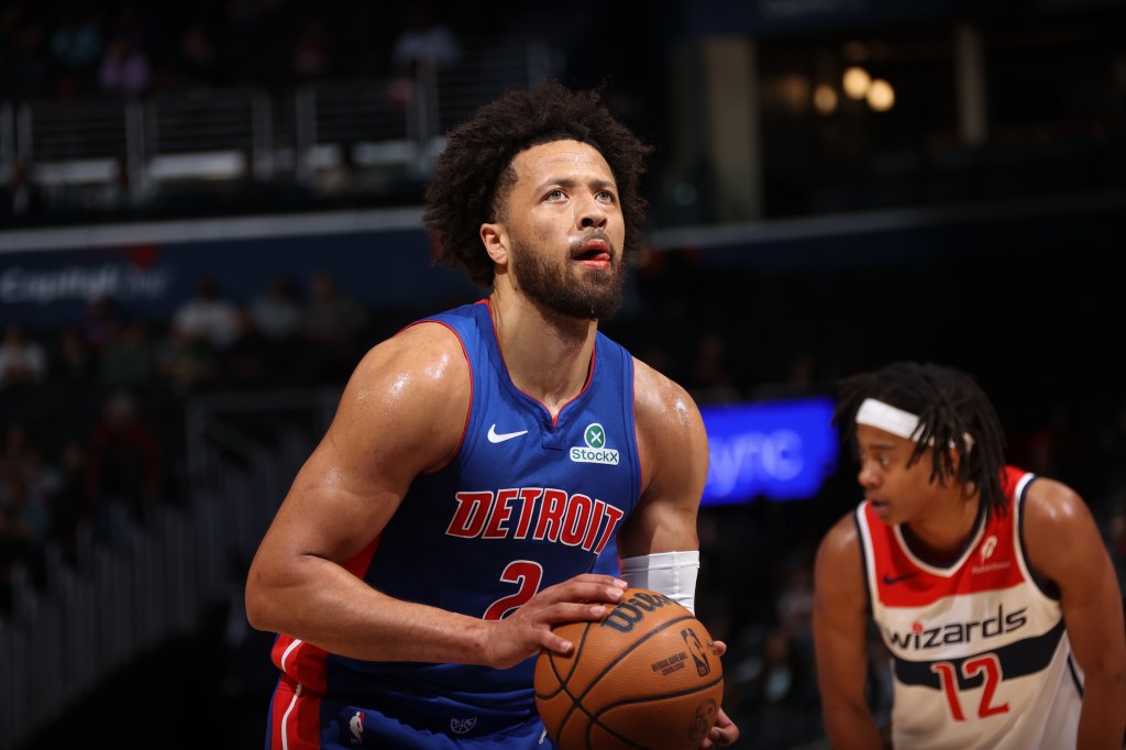 Cade Cunningham, wearing a blue Detroit Pistons jersey, shoots a free throw with a Washington Wizards player in the background.