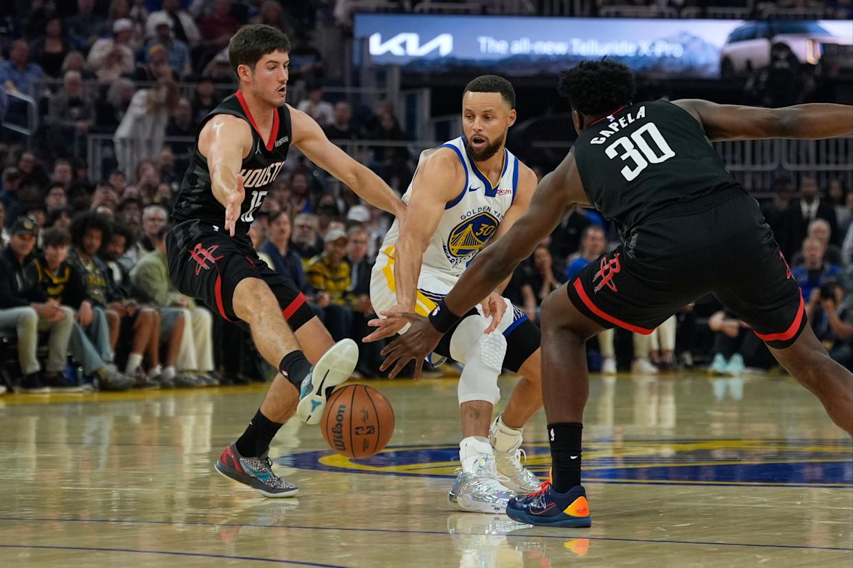 Reed Sheppard kicking a pass by Stephen Curry while Capela watches during an NBA game.