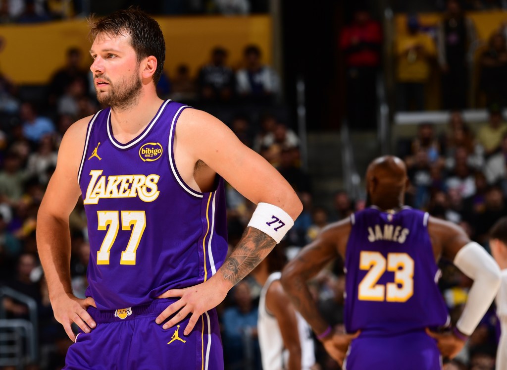 Luka Doncic (number 77) and LeBron James (number 23) in Lakers jerseys look on during a game.