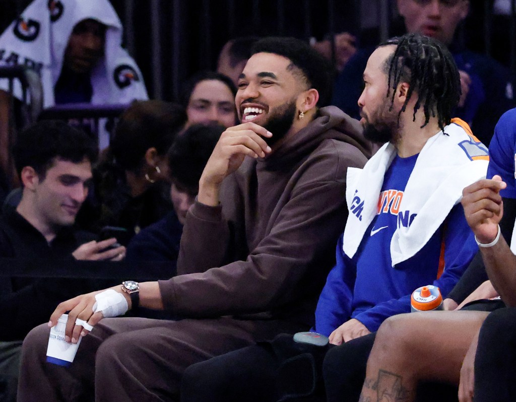 Karl-Anthony Towns #32 of the New York Knicks in plain clothes on the bench jokes around with guard Jalen Brunson #11 of the New York Knicks during the second half against the Bulls.