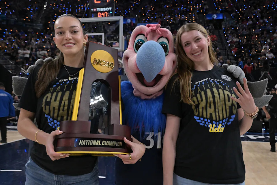 Apr 8, 2026; Inglewood, California, USA; UCLA Bruins womenÕs basketball players Angela Dugalic, holds the National Championship trophy, and Gianna Kneepkens pose with Chuck the Condor as they were honored during a time out at the game between the Los Angeles Clippers and the Oklahoma City Thunder at Intuit Dome. Mandatory Credit: Jayne Kamin-Oncea-Imagn Images