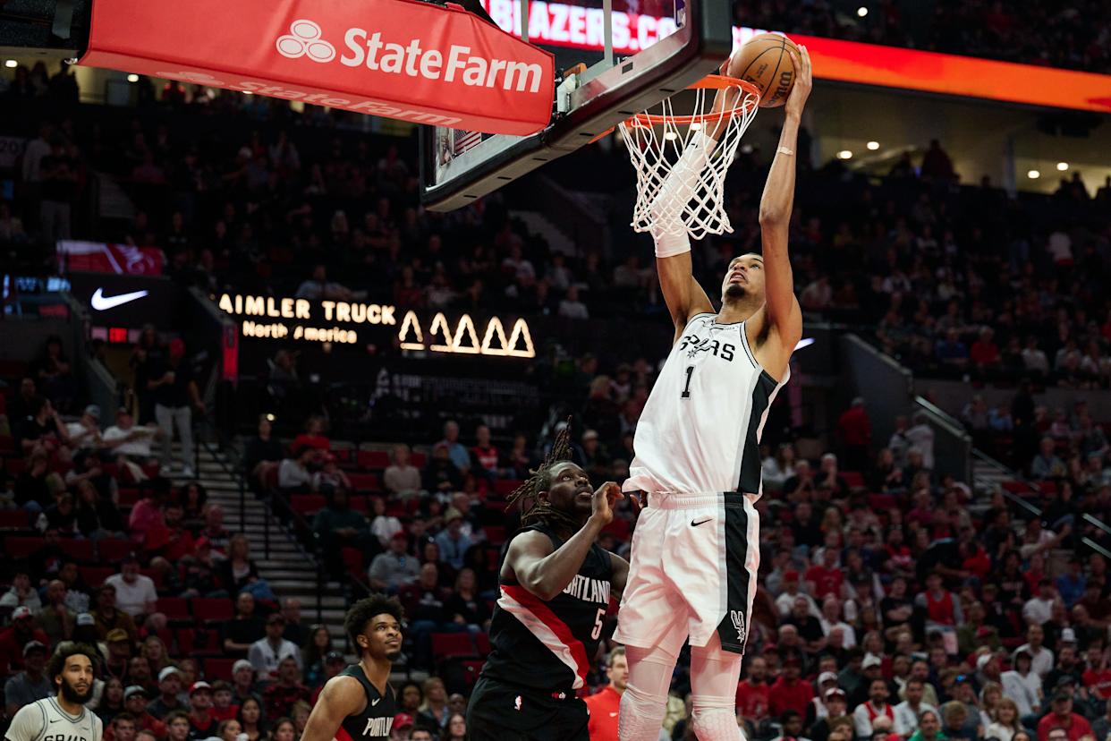 San Antonio Spurs player Victor Wembanyama dunks the basketball as Portland Trail Blazers player Jrue Holiday looks on during a playoff game.