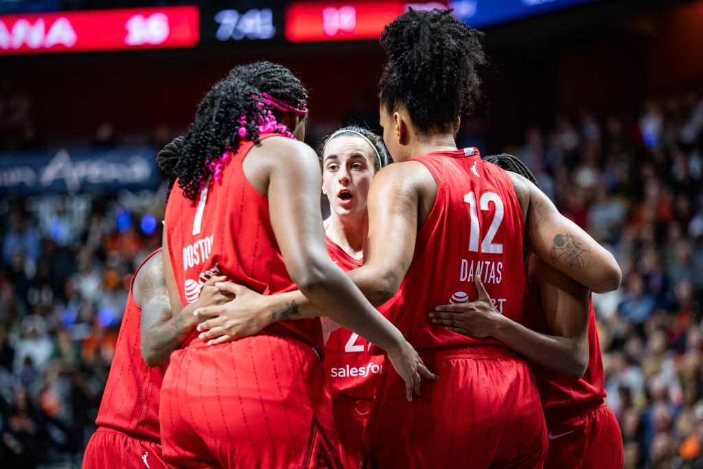 Five Indiana Fever players, all wearing red jerseys, huddle during a game.