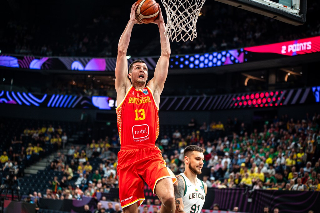 A Montenegro player in a red jersey with number 13 dunks the ball into the hoop during a FIBA EuroBasket 2025 game against Lithuania.