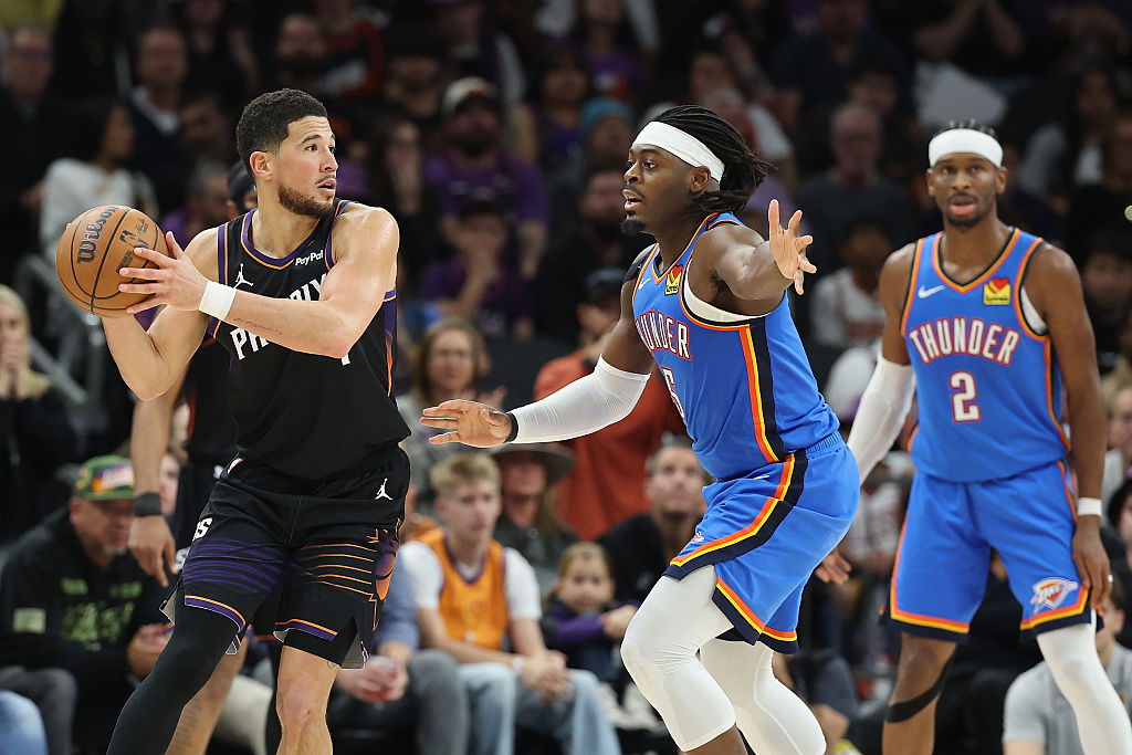 PHOENIX, ARIZONA - JANUARY 04: Devin Booker #1 of the Phoenix Suns looks to pass around Luguentz Dort #5 of the Oklahoma City Thunder during the second half of the NBA game at Mortgage Matchup Center on January 04, 2026 in Phoenix, Arizona. The Suns defeated the Thunder 108-105. NOTE TO USER: User expressly acknowledges and agrees that, by downloading and or using this photograph, user is consenting to the terms and conditions of the Getty Images License Agreement. (Photo by Christian Petersen/Getty Images)