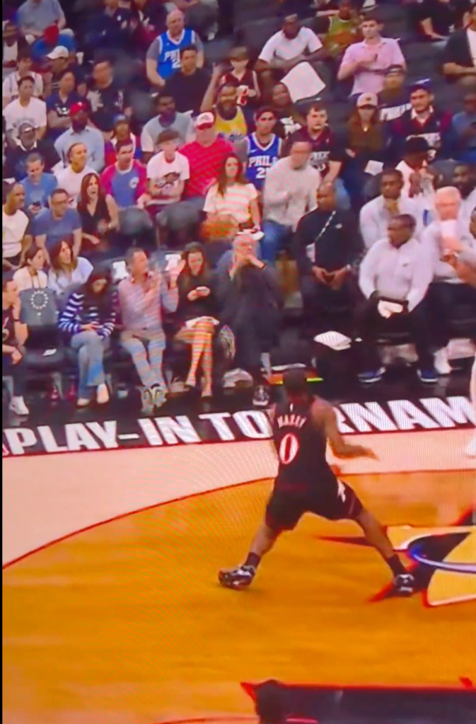 A basketball player in a black jersey with "0" on the back playing on a court with spectators in the background.