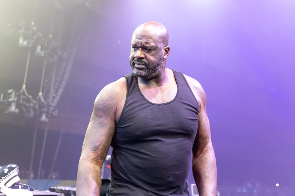 Shaquille O'Neal on stage wearing a black tank top, looking to the side with a focused expression.