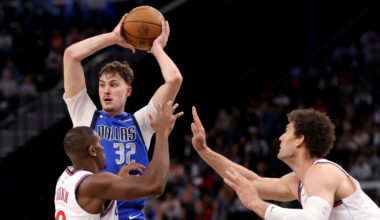 Cooper Flagg #32 of the Dallas Mavericks looks to pass while being guarded by Kris Dunn #8 and Brook Lopez #11 of the Los Angeles Clippers at Intuit Dome.