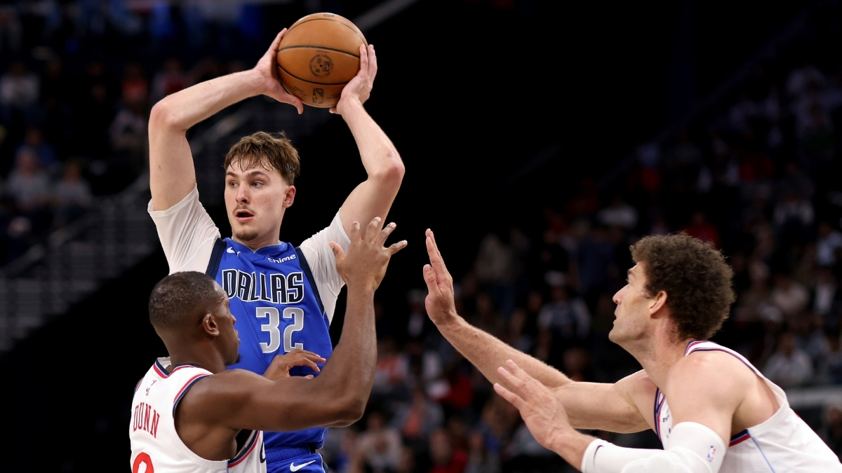 Cooper Flagg #32 of the Dallas Mavericks looks to pass while being guarded by Kris Dunn #8 and Brook Lopez #11 of the Los Angeles Clippers at Intuit Dome.