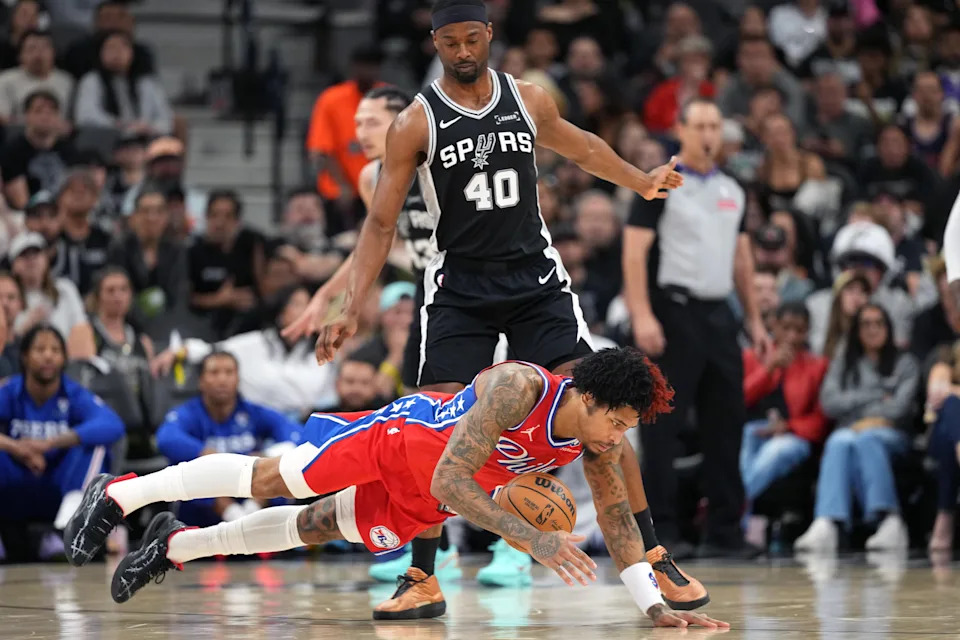 Apr 6, 2026; San Antonio, Texas, USA; Philadelphia 76ers guard Kelly Oubre Jr. (9) falls on a loose ball ahead of San Antonio Spurs forward Harrison Barnes (40) during the first half at Frost Bank Center. Mandatory Credit: Scott Wachter-Imagn Images