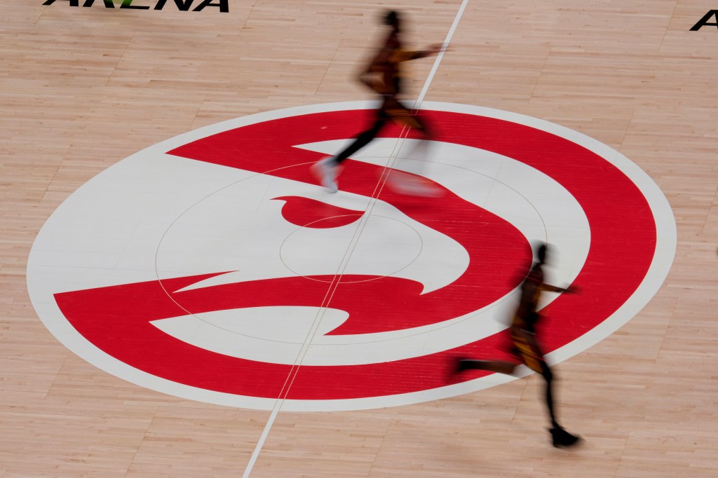Basketball players run past the Atlanta Hawks logo on the court.