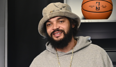 Joakim Noah, wearing a gray hoodie and a bucket hat, is standing indoors with a basketball in the background.