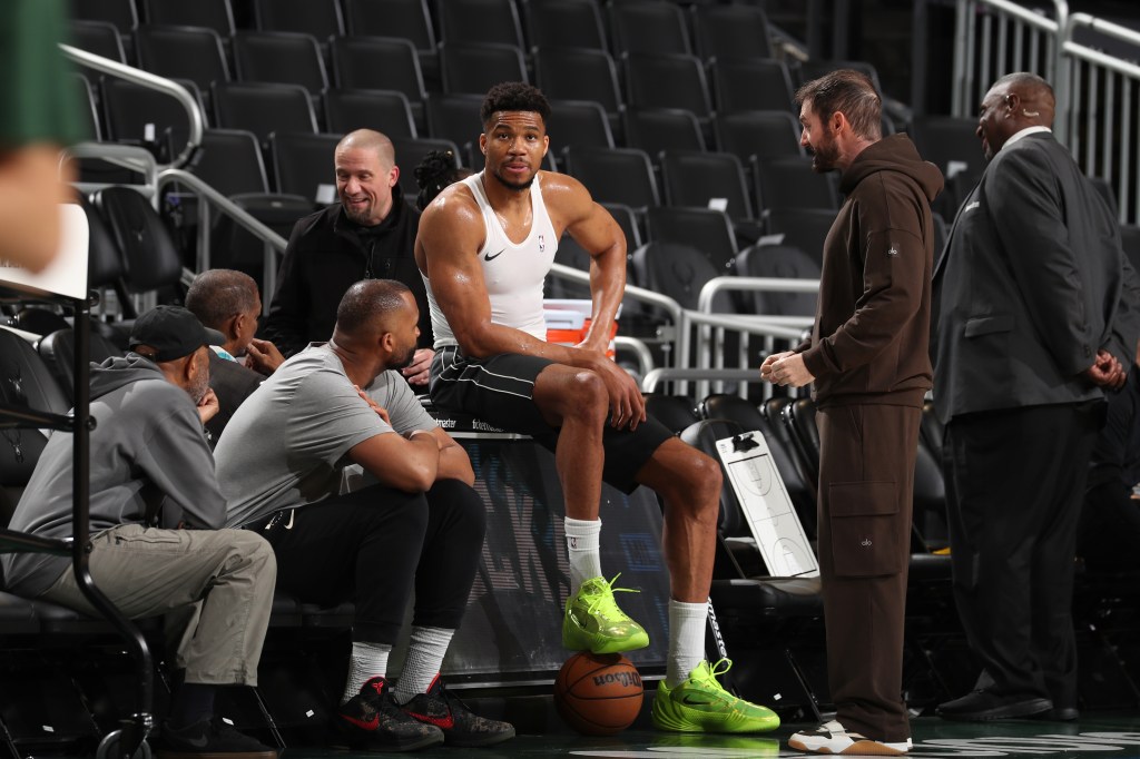 Giannis Antetokounmpo warming up before a game, sitting on a table with one foot on a basketball.