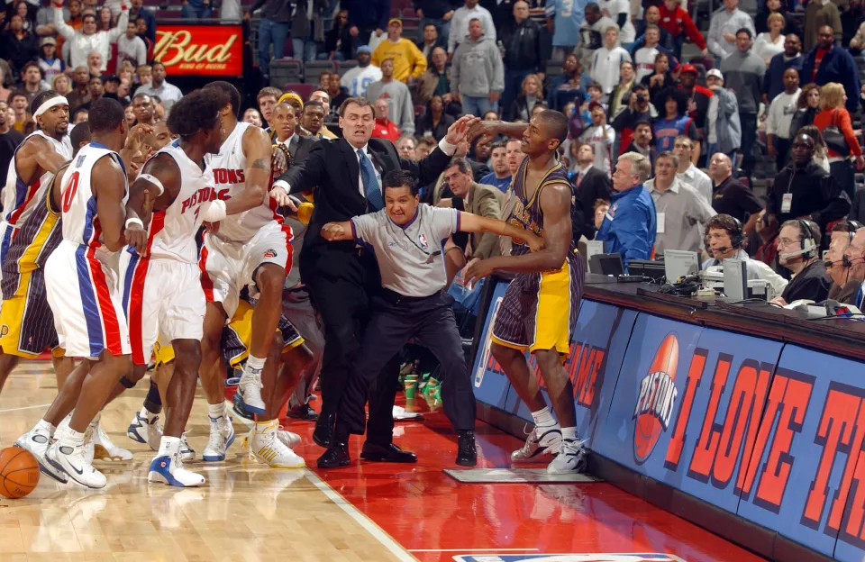 Ben Wallace #3 of the Detroit Pistons and teammates are kept apart from Ron Artest #91 of the Indiana Pacers by Pacers head coach Rick Carlisle and official Tommy Nunez Jr. on November 19, 2004 during their game at the Palace of Auburn Hills in Auburn Hills, Michigan.
