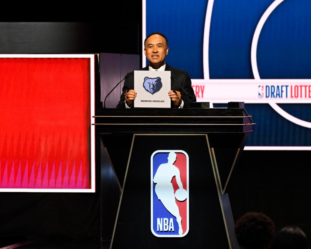 A man in a suit standing at a podium holds up a sign with the Memphis Grizzlies logo.