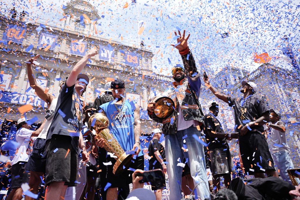 New York Knicks basketball players celebrating with a trophy during a ticker-tape parade as orange and blue confetti falls.