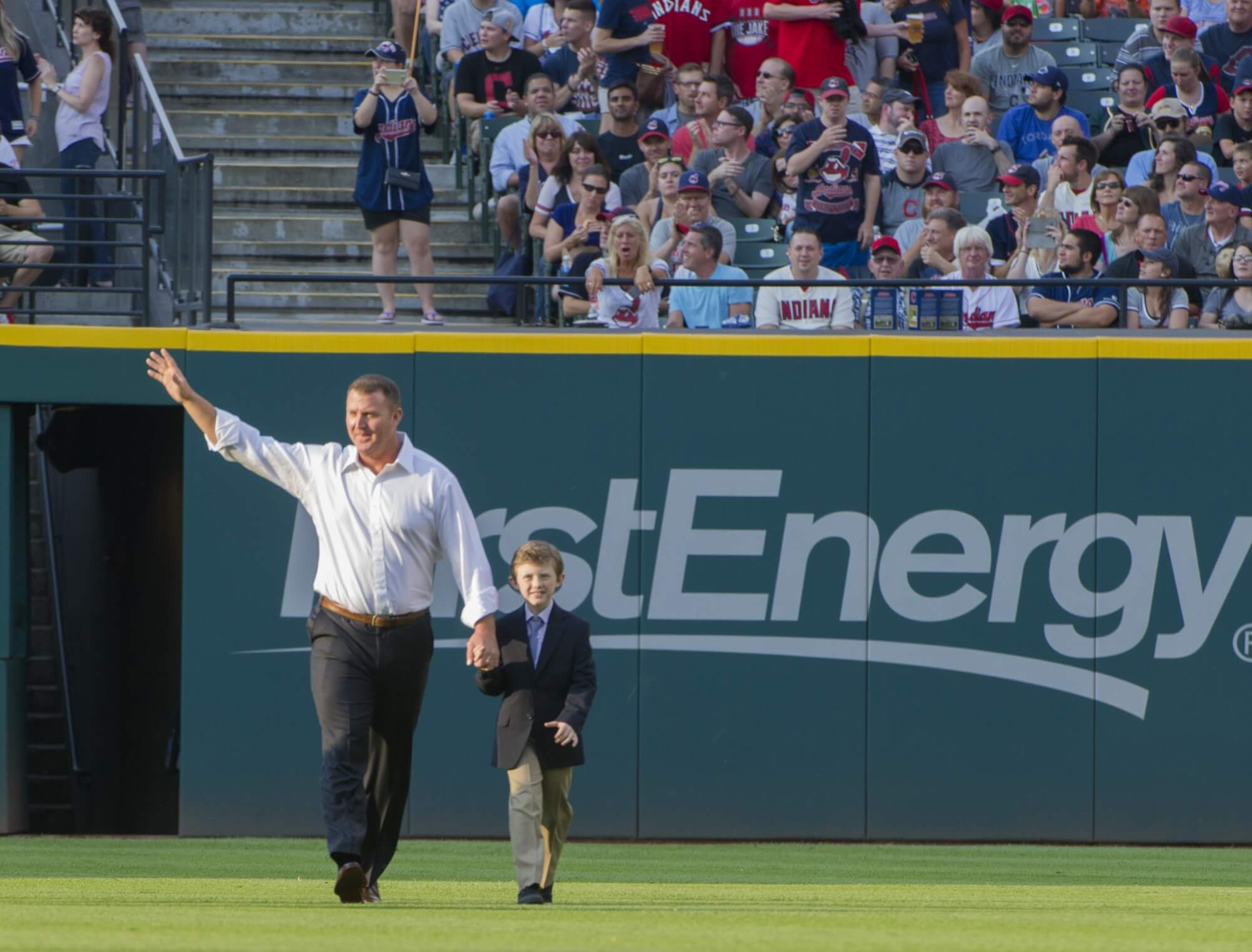 Jim Thome, with right arm raised, walks in the outfield grass toward the infield with his son, Landon.