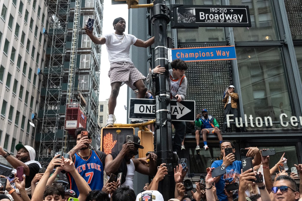 Fans climb a lamp post displaying a "Champions Way" sign during the New York Knicks Championship parade.