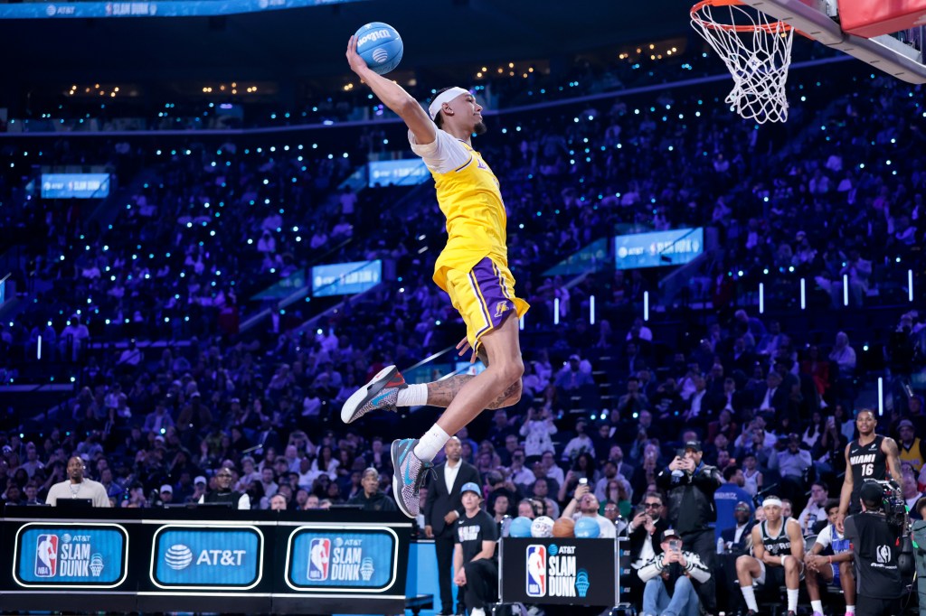 NBA player Mac McClung performs a slam dunk in a yellow and purple uniform.