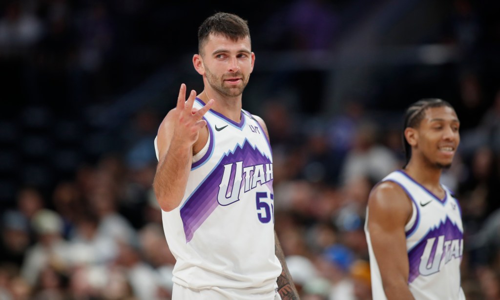 A Utah Jazz player in a white jersey with purple trim holding up three fingers.