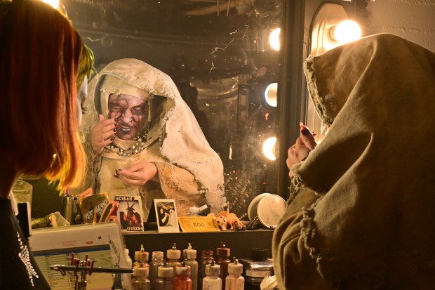 A scare actor dressed as a nun puts contacts in while preparing to perform at the 13th Floor Denver haunted house.
