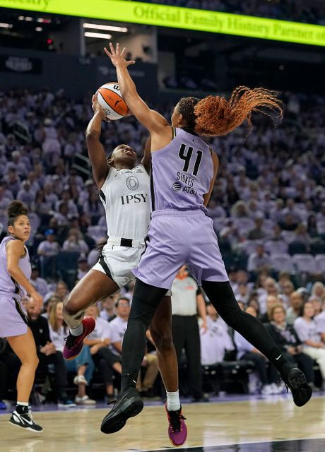 A basketball player in a white uniform leaps to shoot a ball while being defended by a player in a purple uniform numbered 41.
