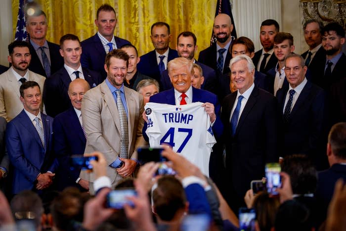 A group of suited individuals with a central figure holding a sports jersey. Event appears formal and celebratory