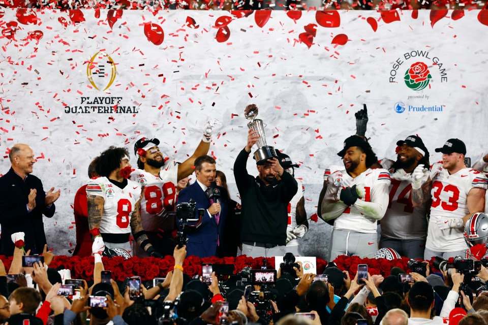 Ohio State Buckeyes head coach Ryan Day holding the Rose Bowl trophy with his team.
