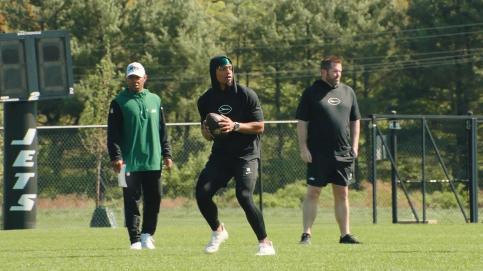 A football player practicing on a field with two coaches.