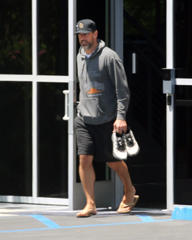Aaron Rodgers leaving a building, carrying his shoes.