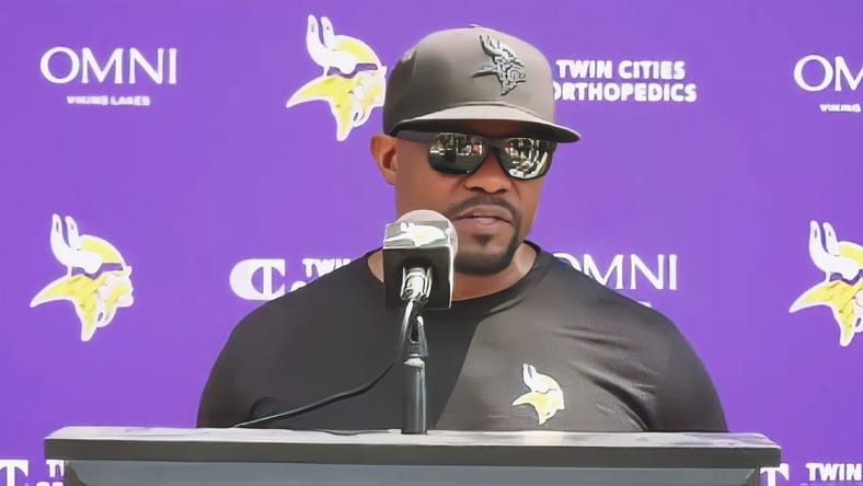 Brian Flores speaks to reporters at Vikings training camp. vikings offseason surprises 2026